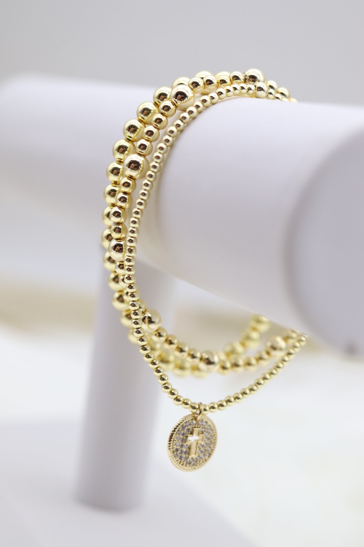 Triple Layered Gold Beaded Bracelet With Smaller Cross Dangling Pendant
